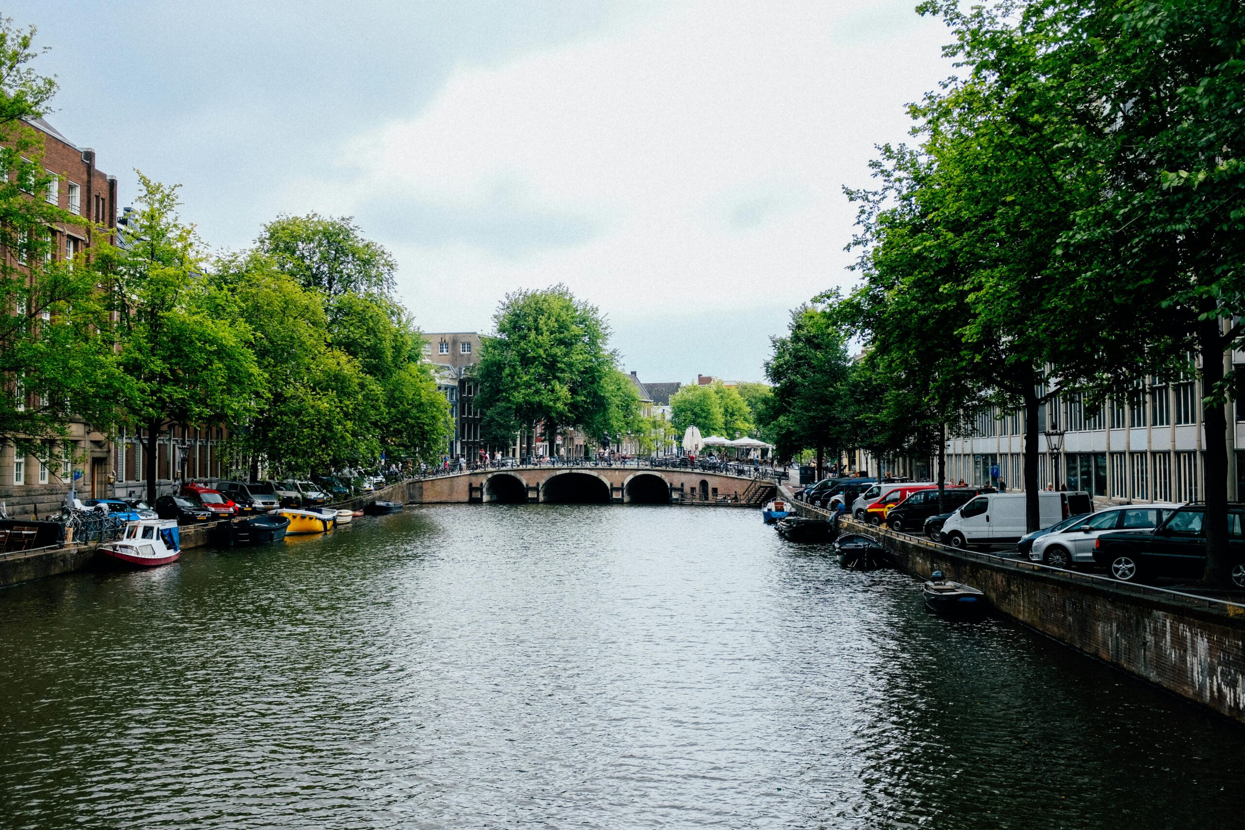 Peaceful canal view in Amsterdam featuring lush trees, boats, and historic buildings.